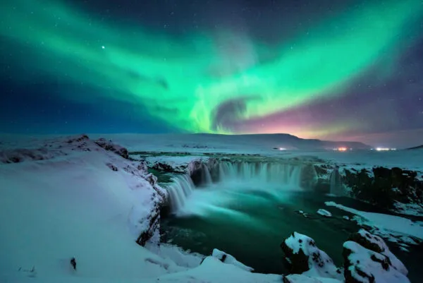 Uitzicht op de Godafoss-waterval in IJsland met een groen-paarse lucht van het Noorderlicht