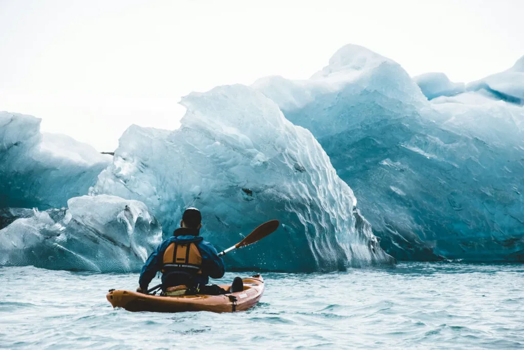 Een reiziger kajakt tussen ijsschotsen van het Jökulsárlón-gletsjermeer in IJsland