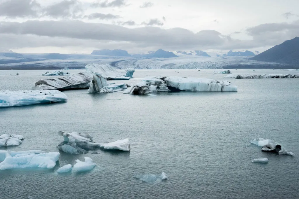 Grote blauw-witte ijsbergen drijven rustig op het gletsjermeer Jökulsárlón met besneeuwde bergen op de achtergrond in IJsland.