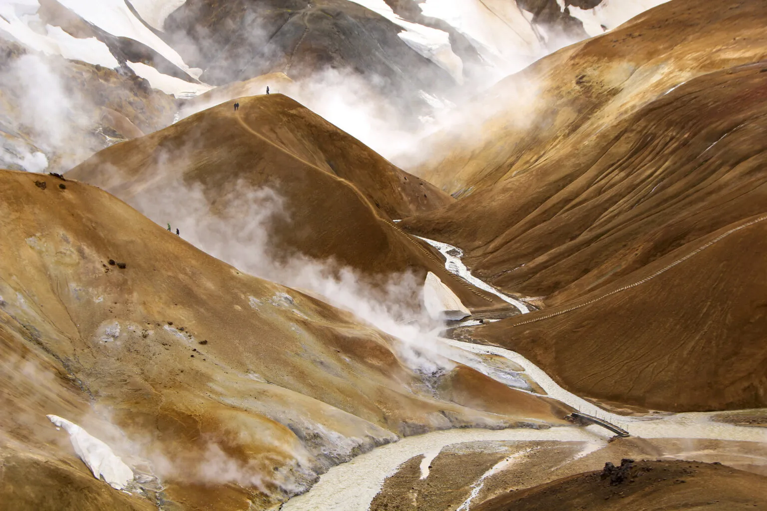 Zicht op de stoomwolken die opstijgen uit het geothermische gebied Hveradalir tussen de oranjebruine rijolietbergen van Kerlingarfjöll in IJsland.