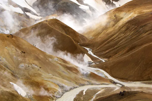 Zicht op de stoomwolken die opstijgen uit het geothermische gebied Hveradalir tussen de oranjebruine rijolietbergen van Kerlingarfjöll in IJsland.