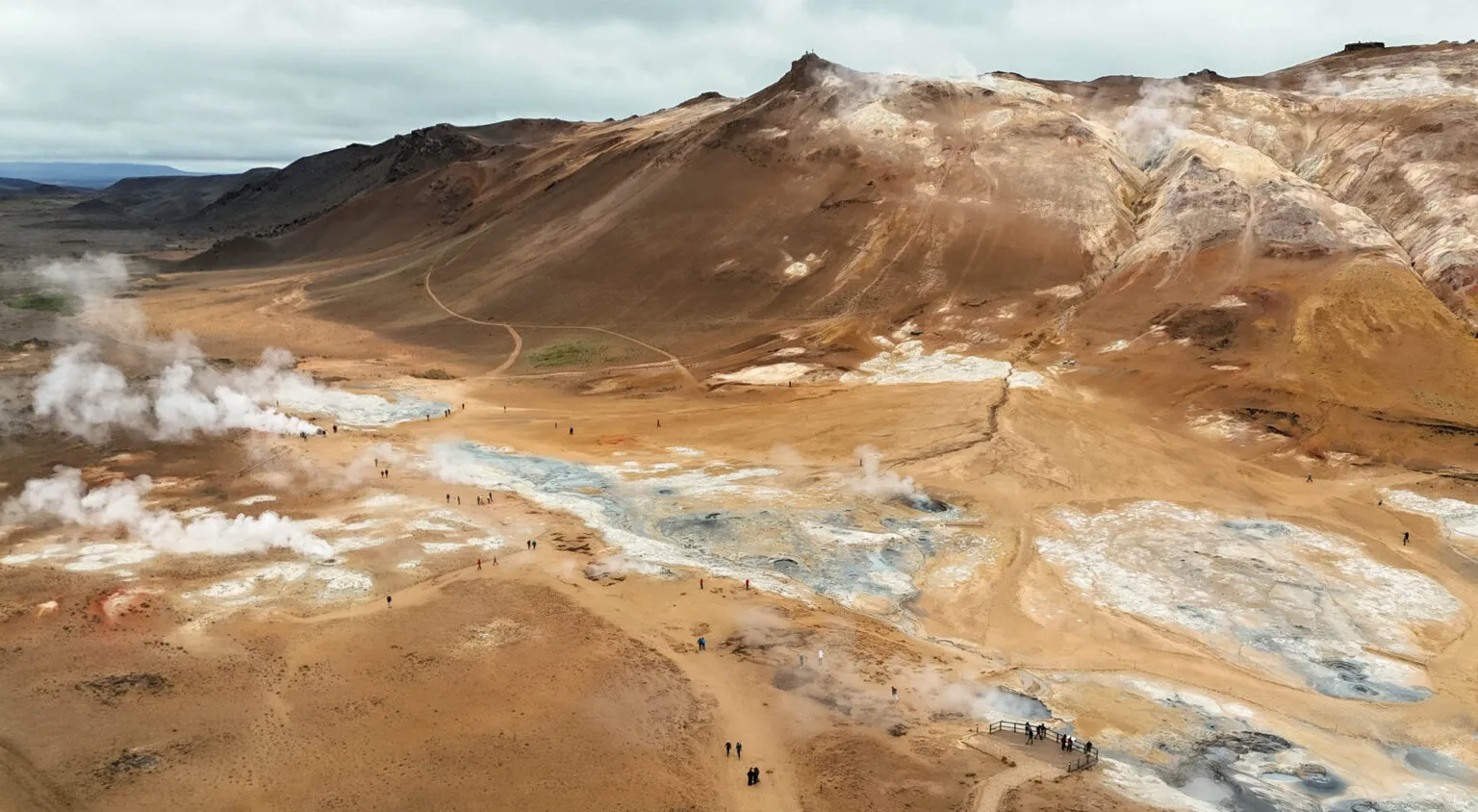 Panoramisch bovenaanzicht van het okergele, buitenaardse landschap van Hverir bij Mývatn in IJsland, met rokende stoompluggen, modderpotten en wandelpaden langs de berghelling.
