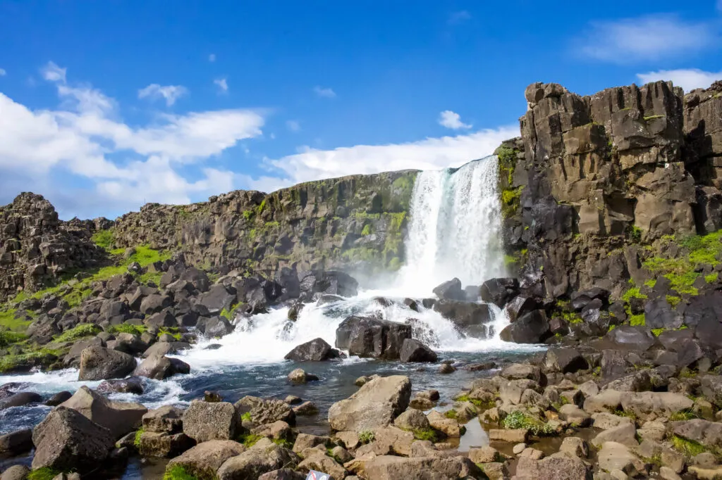 De Öxarárfoss waterval stroomt over donkere rotsen in de ruige kloof van Nationaal Park Þingvellir onder een heldere blauwe lucht in IJsland