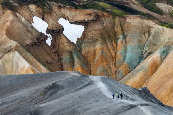 Een groepje reizigers hikt over een asgrijze bergrug voor de kleurrijke vulkanische bergen van Landmannalaugar in natuurreservaat Fjallabak.