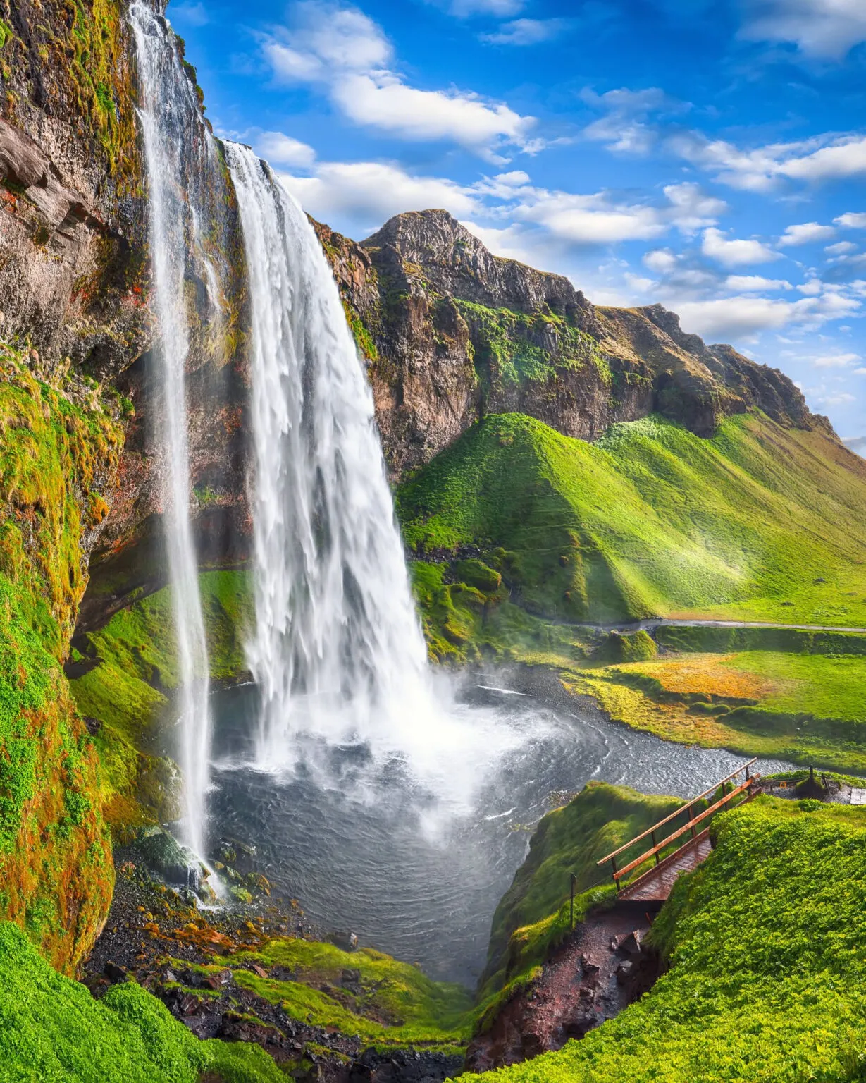 De indrukwekkende Seljalandsfoss waterval klettert langs een steile rotswand naar beneden in het groene landschap van IJsland.