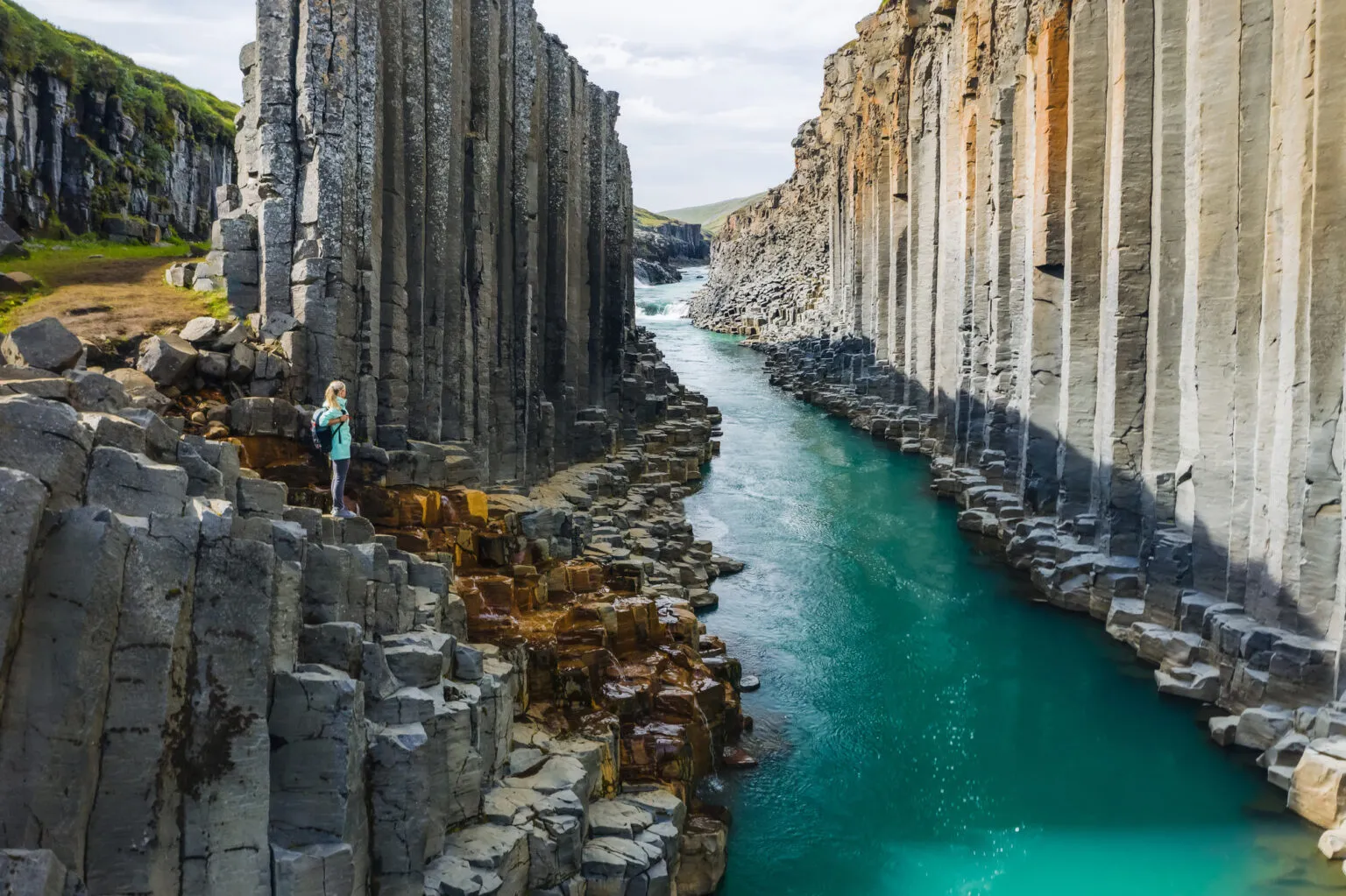 Een vrouwelijke reiziger staat tussen de indrukwekkende basaltkolommen van de Stuðlagil Canyon langs een turkooisblauwe rivier in IJsland.