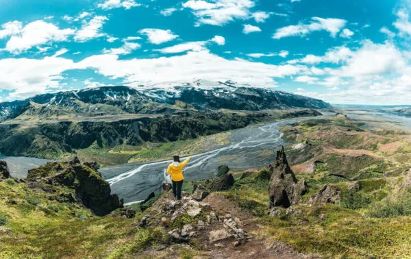 Een vrouwelijke reiziger kijkt uit over het indrukwekkende berglandschap van Þórsmörk vanaf het uitzichtpunt op de berg Valahnúkur in IJsland.