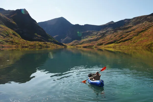 Een man kajakt in een blauwe kajak over stil water in een fjord omgeven door steile bergen nabij Ísafjörður in de Westfjorden van IJsland.