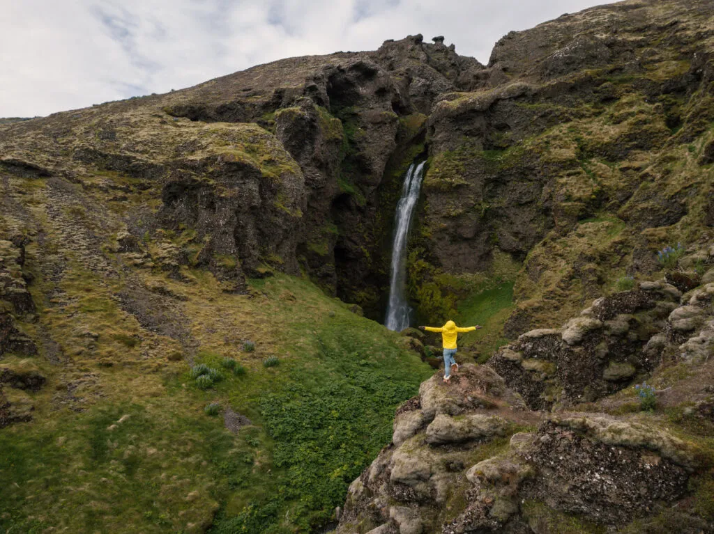 Een vrouwelijke reiziger staat op een rots langs de Valagil trail bij een waterval in de Westfjorden van IJsland.