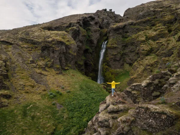 Een vrouwelijke reiziger staat op een rots langs de Valagil trail bij een waterval in de Westfjorden van IJsland.