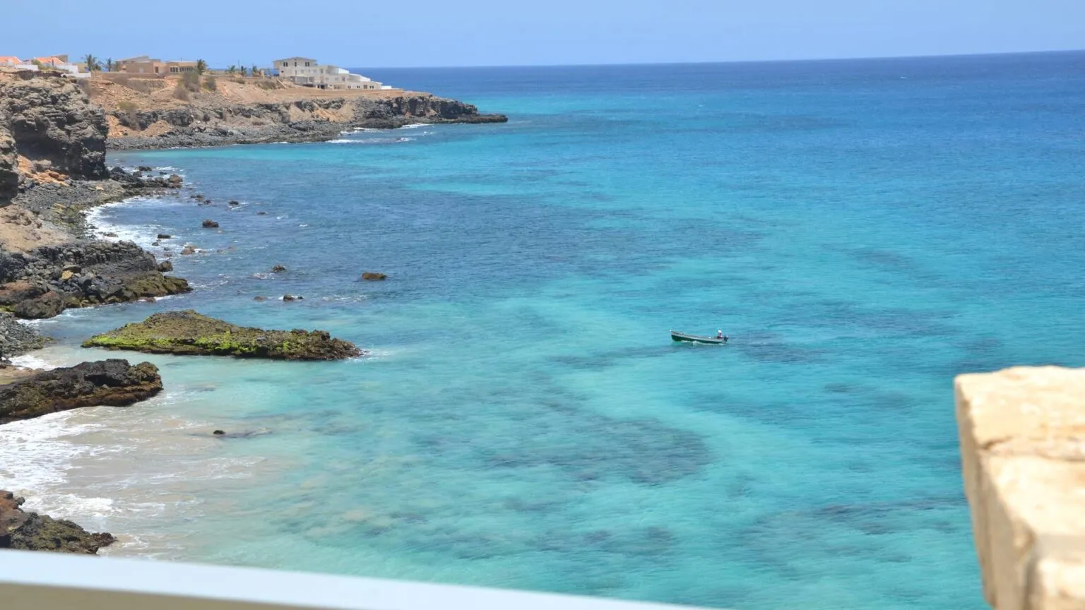 Uitzicht vanaf Casa Amarella op een helderblauwe baai met turquoise water en rotsachtige kustlijn in Vila do Maio op het eiland Maio.