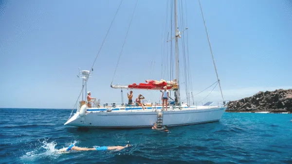 Reizigers op het dek van een witte zeilboot en iemand die zwemt in het heldere zeewater bij het eiland Sal, Kaapverdië.