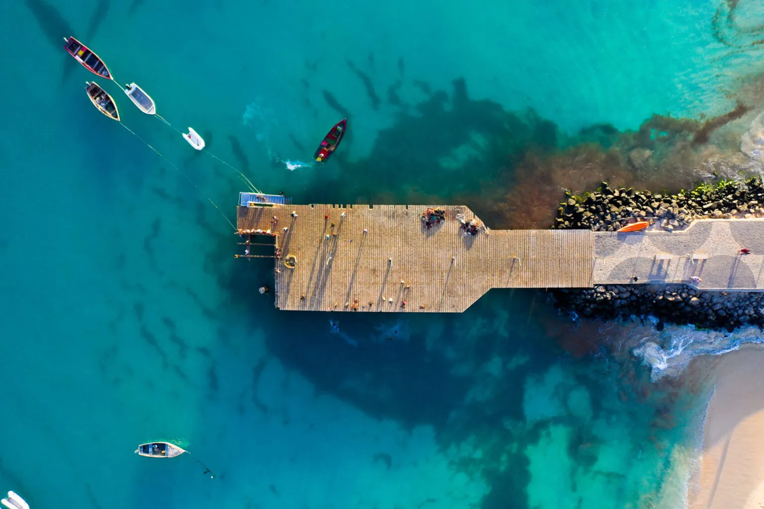 Bovenaanzicht van de stenen pier van Santa Maria omgeven door helderblauw water en dobberende bootjes op het eiland Sal, Kaapverdië.