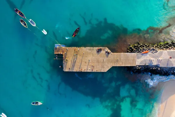 Bovenaanzicht van de stenen pier van Santa Maria omgeven door helderblauw water en dobberende bootjes op het eiland Sal, Kaapverdië.