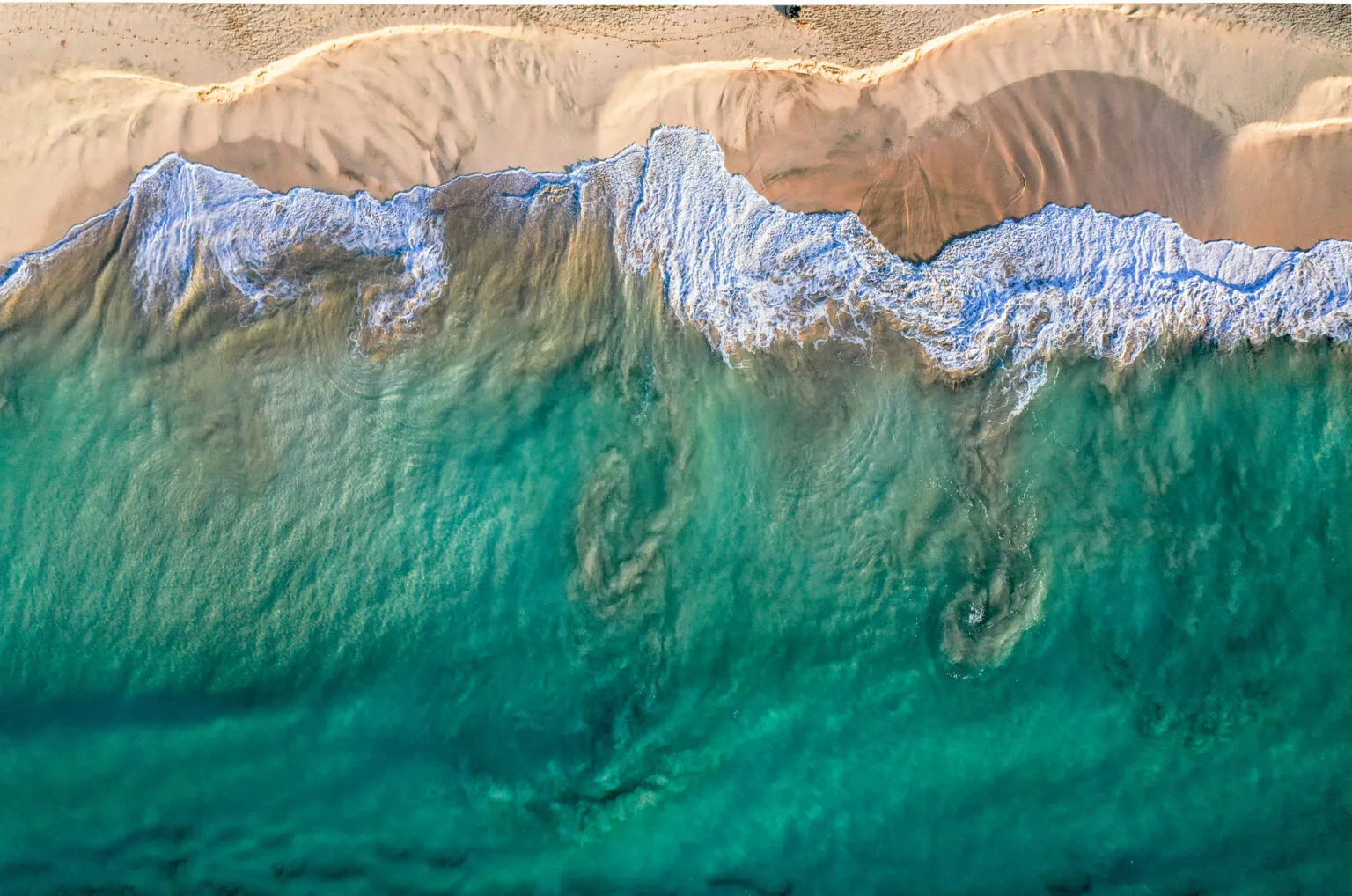 Aanzicht van bovenaf van helderblauw zeewater met schuimende golven die aanspoelen op een goudgeel zandstrand op Kaapverdië.