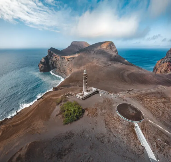 Perspectief van het uitgestrekte vulkanische landschap van Capelinhos op Faial, met de eenzame vuurtoren te midden van asvelden aan de oceaan.