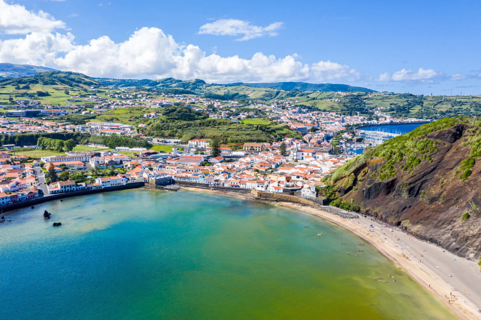 De baai en het zandstrand van Porto Pim met de kuststad Horta en groene heuvels op het eiland Faial in de Azoren