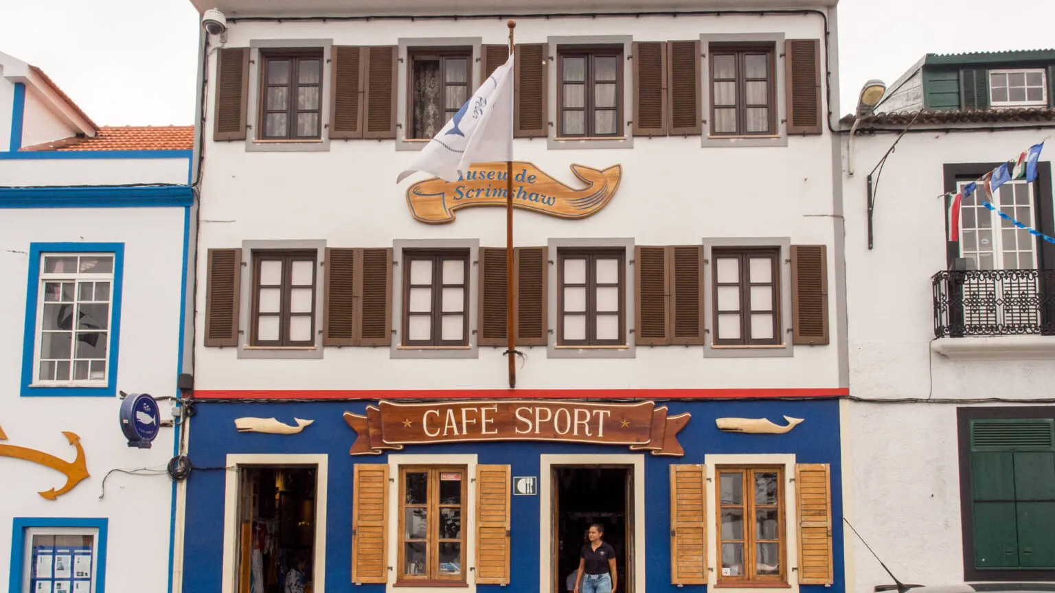 Gevel van het iconische Peter Café Sport met een blauwe onderpui, bruine houten luiken en een houten walvisbord in Horta op het eiland Faial in de Azoren