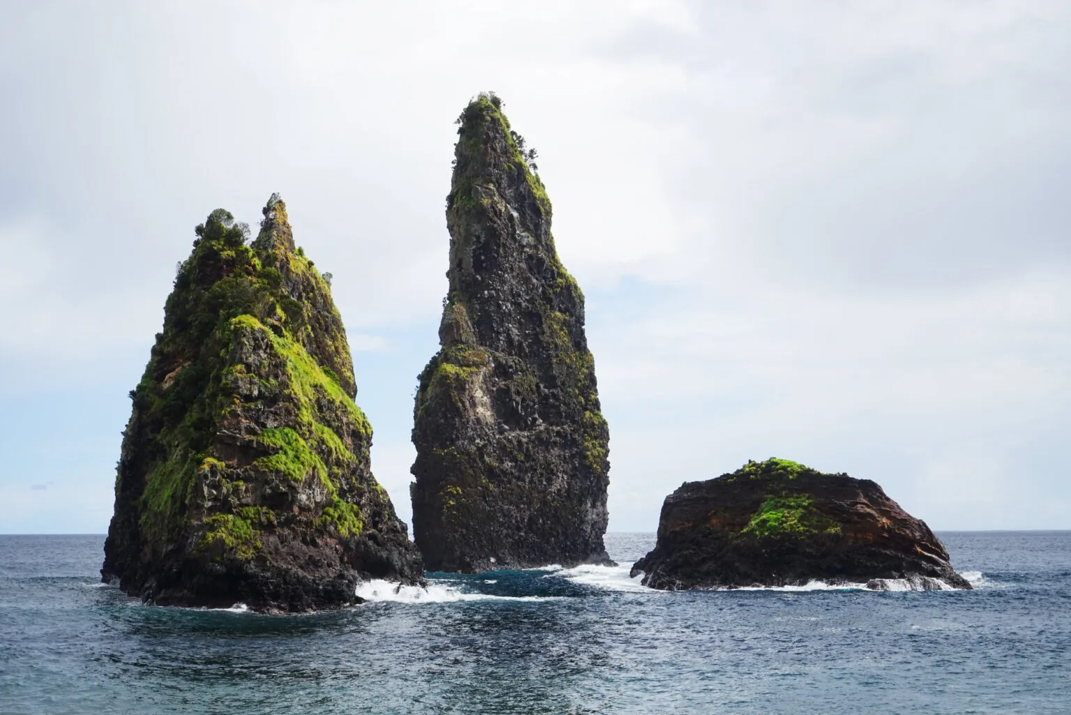 Met mos begroeide, steil oprijzende vulkanische rotspilaren die uit de azuurblauwe oceaan omhoogkomen voor de kust van het eiland Flores op de Azoren.