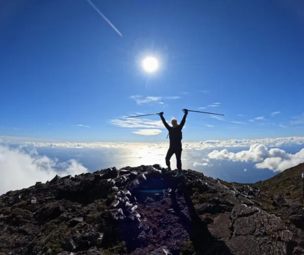 Silhouet van een vrouw met wandelstokken op de rotsachtige top van de vulkaan Pico boven het wolkendek in de Azoren