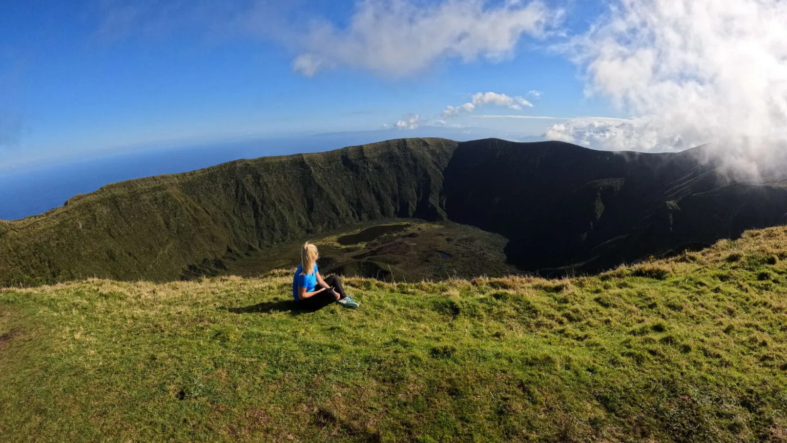 Reiziger zit in het gras op de rand van een grote vulkaankrater en geniet van het panoramische uitzicht op Caldeira do Faial op het eiland Faial, Azoren.