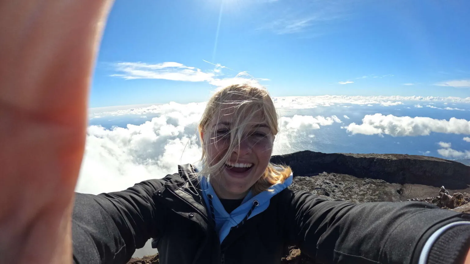 Een glimlachende vrouwelijke reiziger maakt een selfie op de bergtop van Mount Pico, met een uitzicht over de wolken en de oceaan op de Azoren.