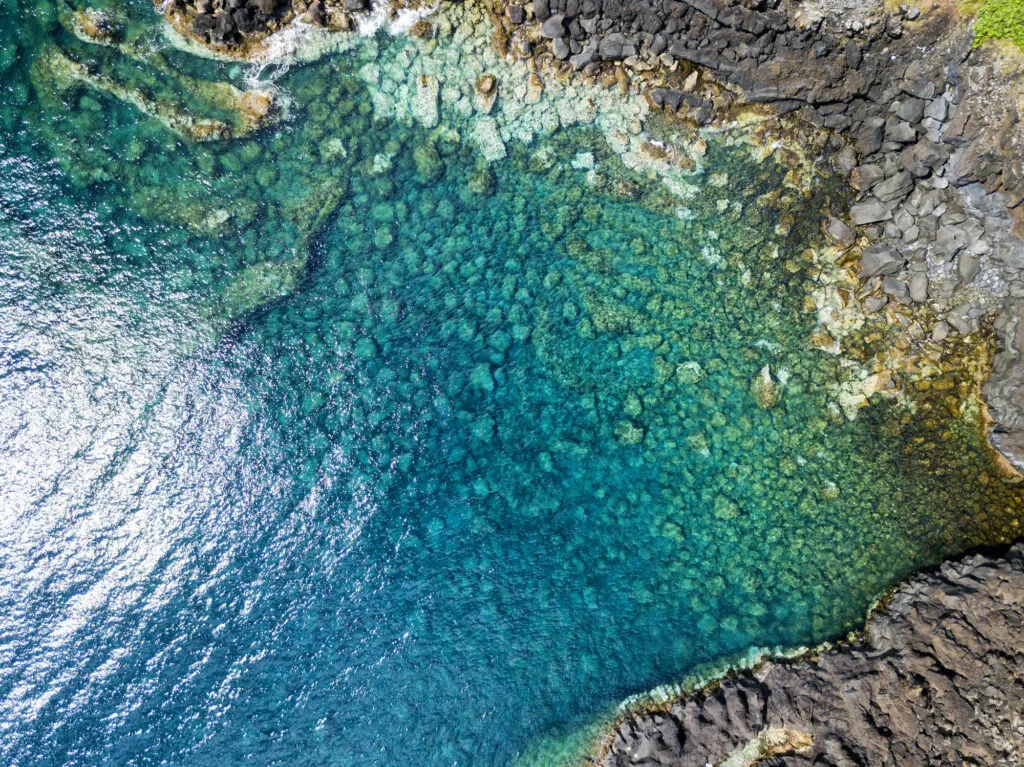 Aanzicht van bovenaf op het heldere, azuurblauwe water en de ruige rotskust bij Canada de África op het eiland São Jorge in de Azoren.