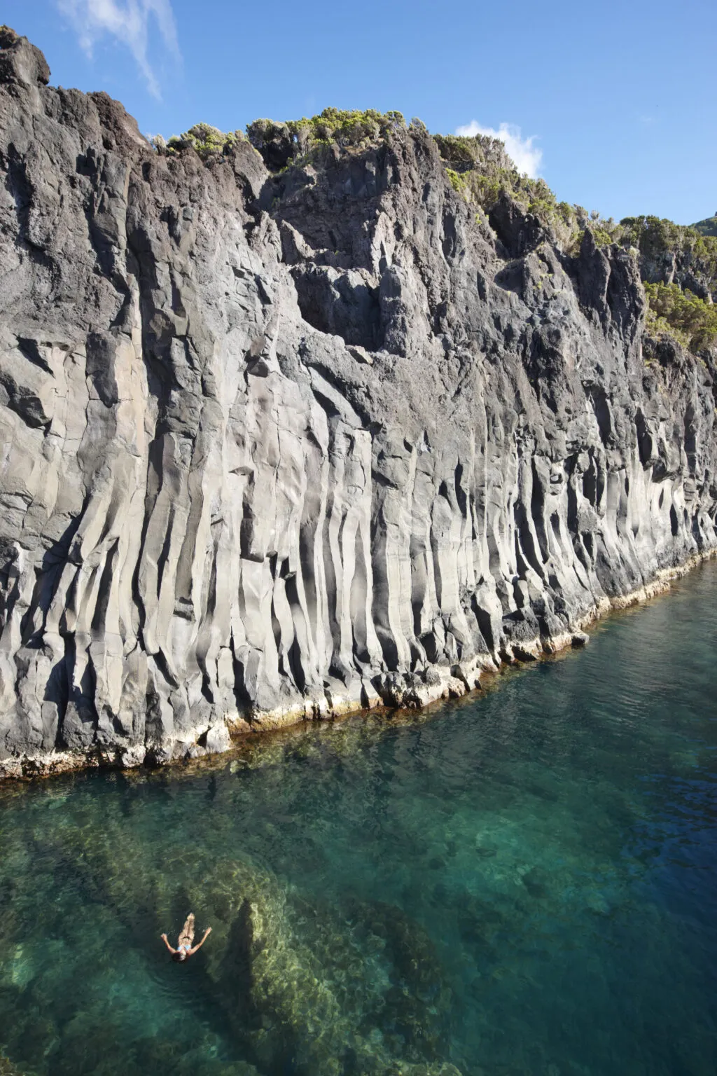 Een vrouw zwemt in het heldere water van het natuurlijke rotszwembad van Fajã do Ouvidor op São Jorge, omgeven door steile vulkanische rotswanden.