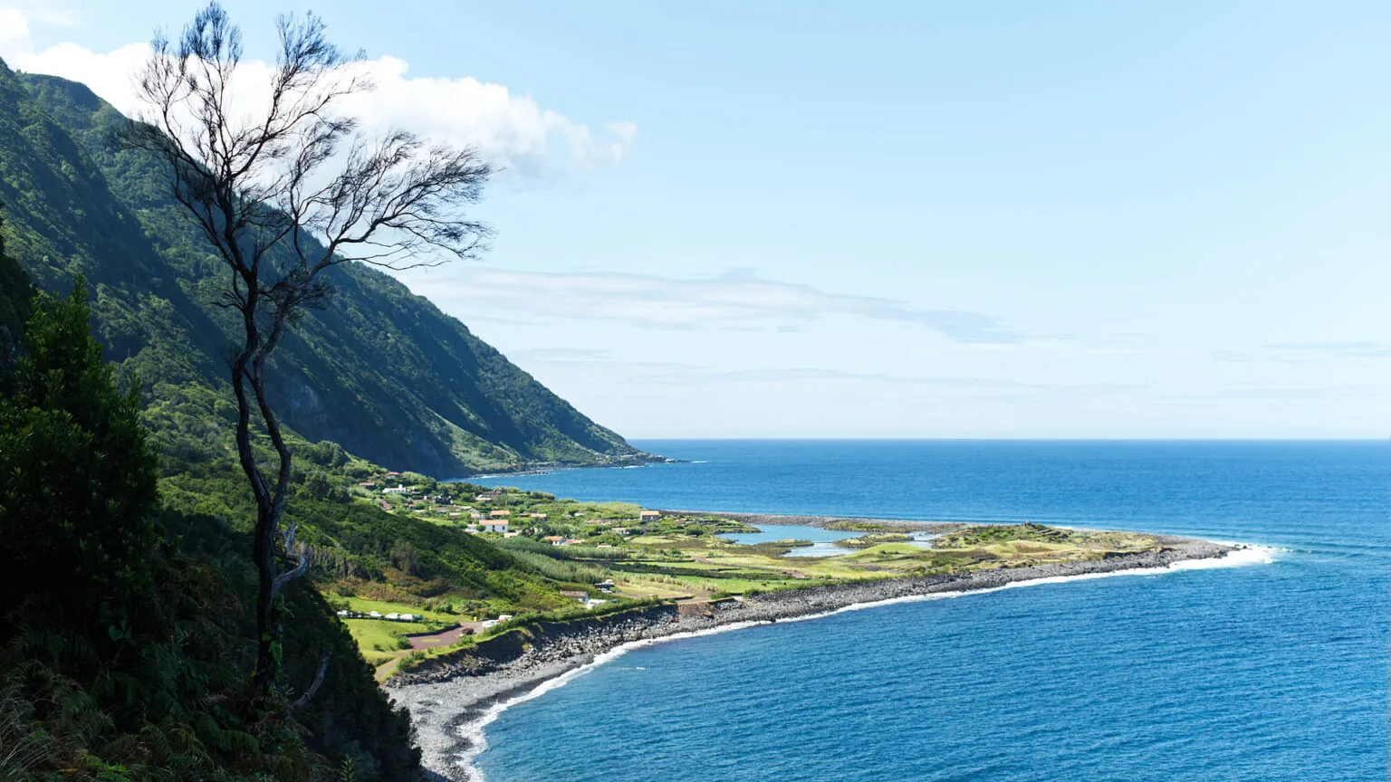 Panoramisch zicht van bovenaf op de kustvlakte van Fajã dos Cubres met haar lagune, omgeven door steile groene bergwanden en de diepblauwe oceaan op São Jorge.