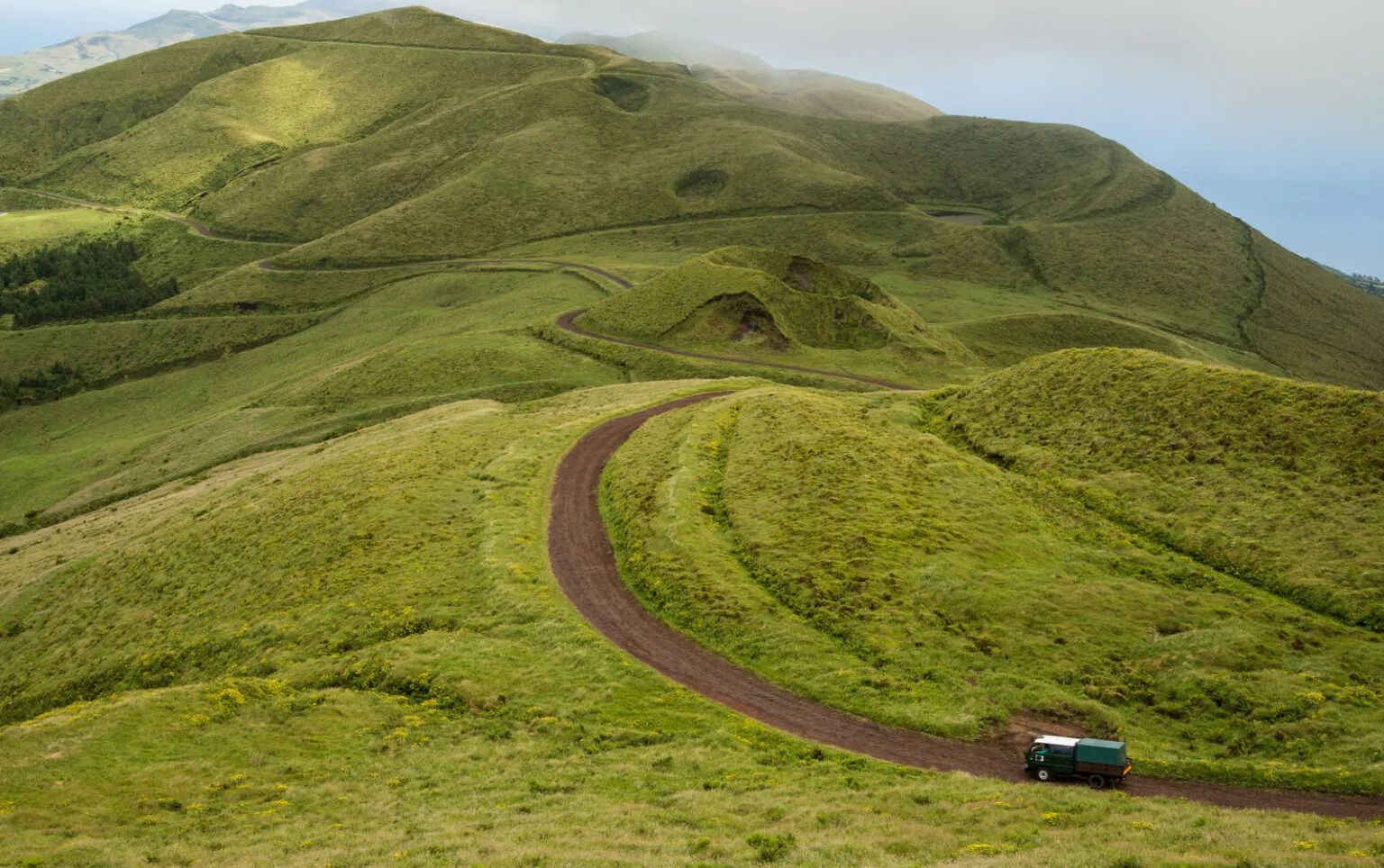 Een rode asfaltweg slingert door glooiende, groene vulkanische heuvels met een auto in het landschap op São Jorge in de Azoren.