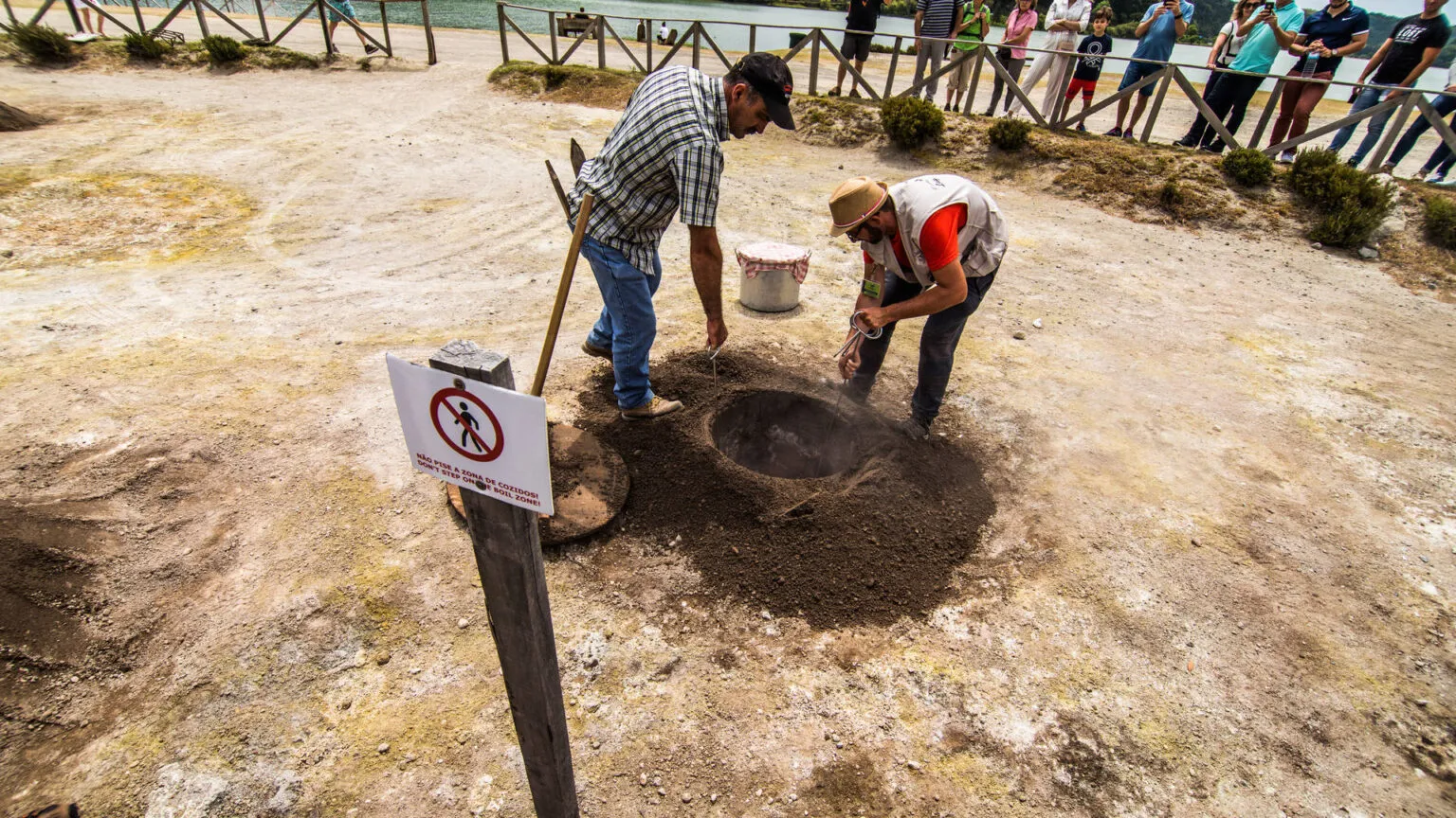 Twee personen halen een kookpot uit de vulkanisch verwarmde grond bij de stoombronnen van Furnas op het eiland São Miguel.