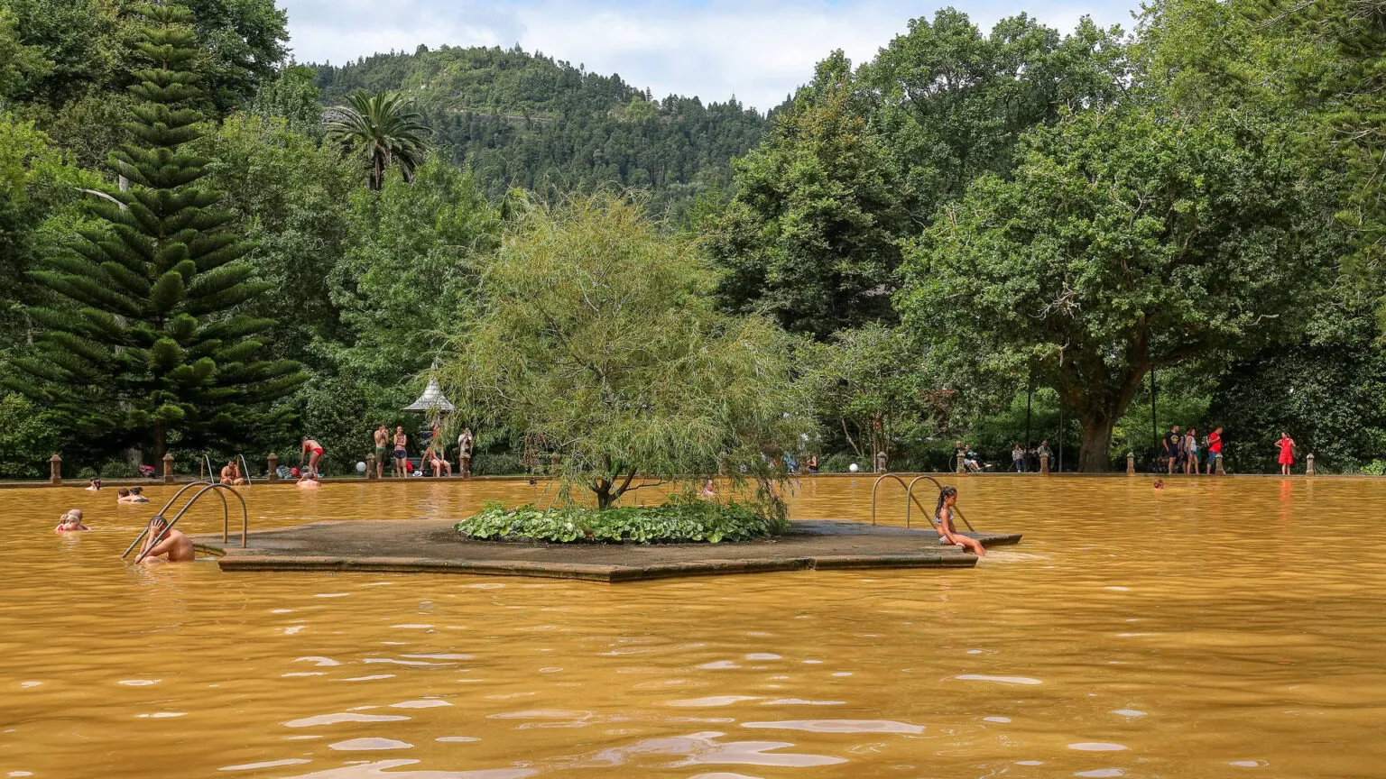 Mensen zwemmen in het oranjegeel, ijzerrijke thermale bad van Parque Terra Nostra, omgeven door weelderige groene bomen in Furnas op São Miguel.