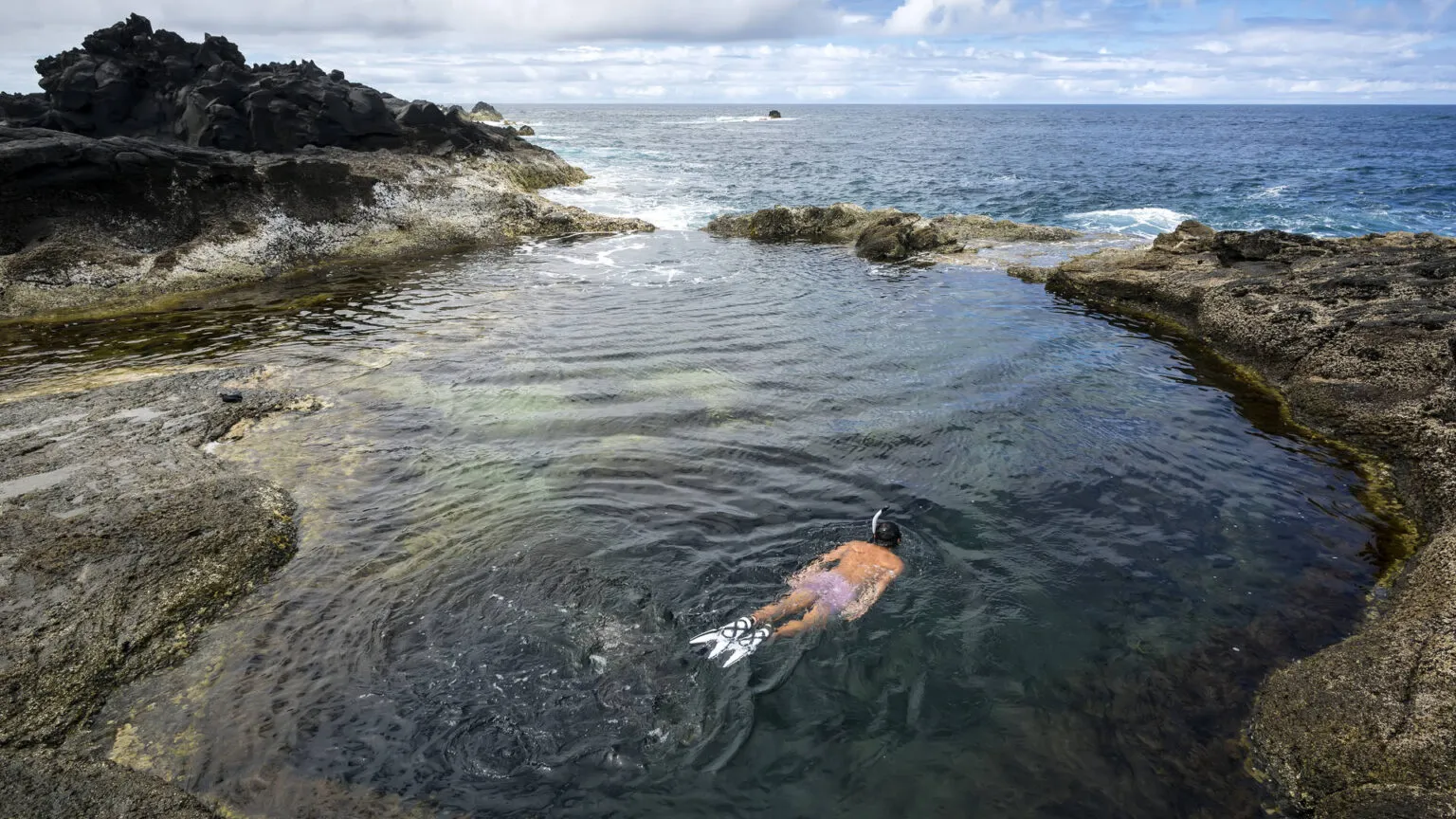 Bovenaanzicht van iemand die snorkelt in het heldere water van een natuurlijk lavarotszwembad aan de kust bij Mosteiros op São Miguel, Azoren.