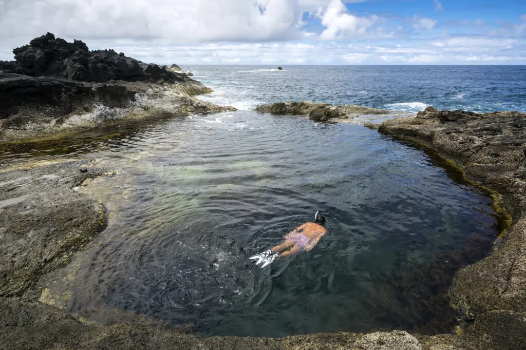Een persoon snorkelt in een helder, natuurlijk rotszwembad gevuld met zeewater aan de kust van Mosteiros op het eiland São Miguel.