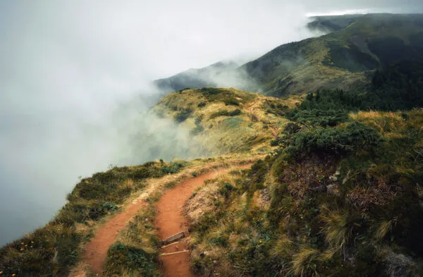 Smal onverhard wandelpad dat over een groene bergkam slingert, half gehuld in dichte mist in het berglandschap van São Miguel op de Azoren