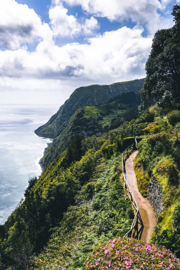 Een kronkelend wandelpad langs steile groene kliffen vol bloemen en planten met uitzicht op de Atlantische Oceaan bij Ponta do Sossego.