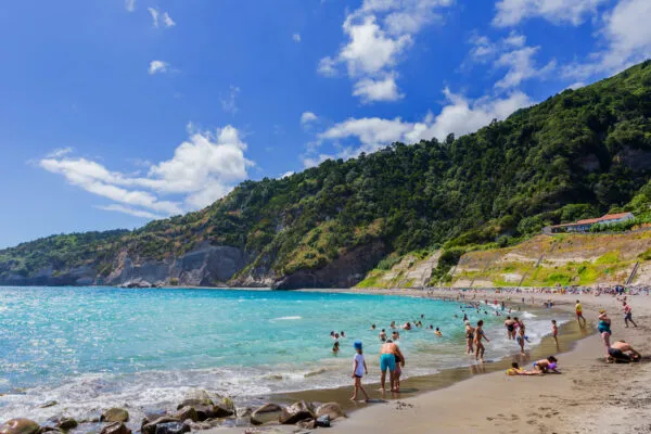 Badgasten genieten van het heldere zeewater op een zandstrand nabij Ribeira Quente, beschut door steile groene bergen.