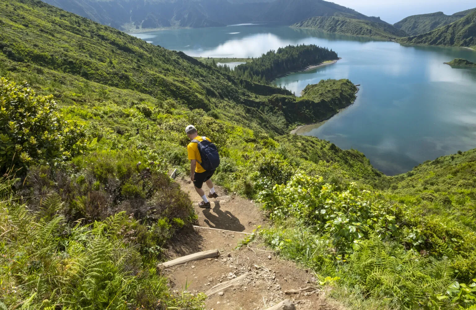 Wandelaar met rugzak loopt over een zandpad naar het kratermeer Lagoa do Fogo op het eiland São Miguel in de Azoren