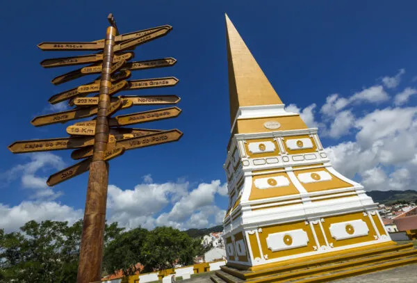 De opvallende geel met witte obelisk Alto da Memória en een houten wegwijzer met pijlborjes tegen een helderblauwe lucht in Angra do Heroísmo op het eiland Terceira.