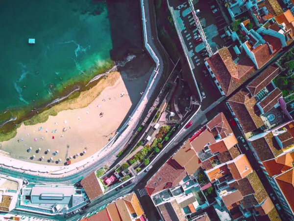 Bovenaanzicht van het zandstrand Prainha de Angra met helder turquoise water, aangrenzend aan de kade en gebouwen van Angra do Heroísmo op Terceira.