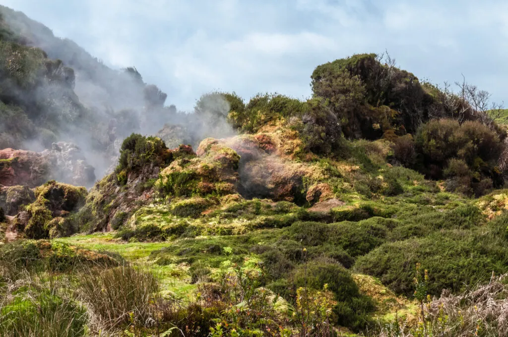 Witte stoom pluimen stijgen op uit de met mos begroeide, vulkanische rotsen van het geotermische gebied Furnas do Enxofre op Terceira in de Azoren.