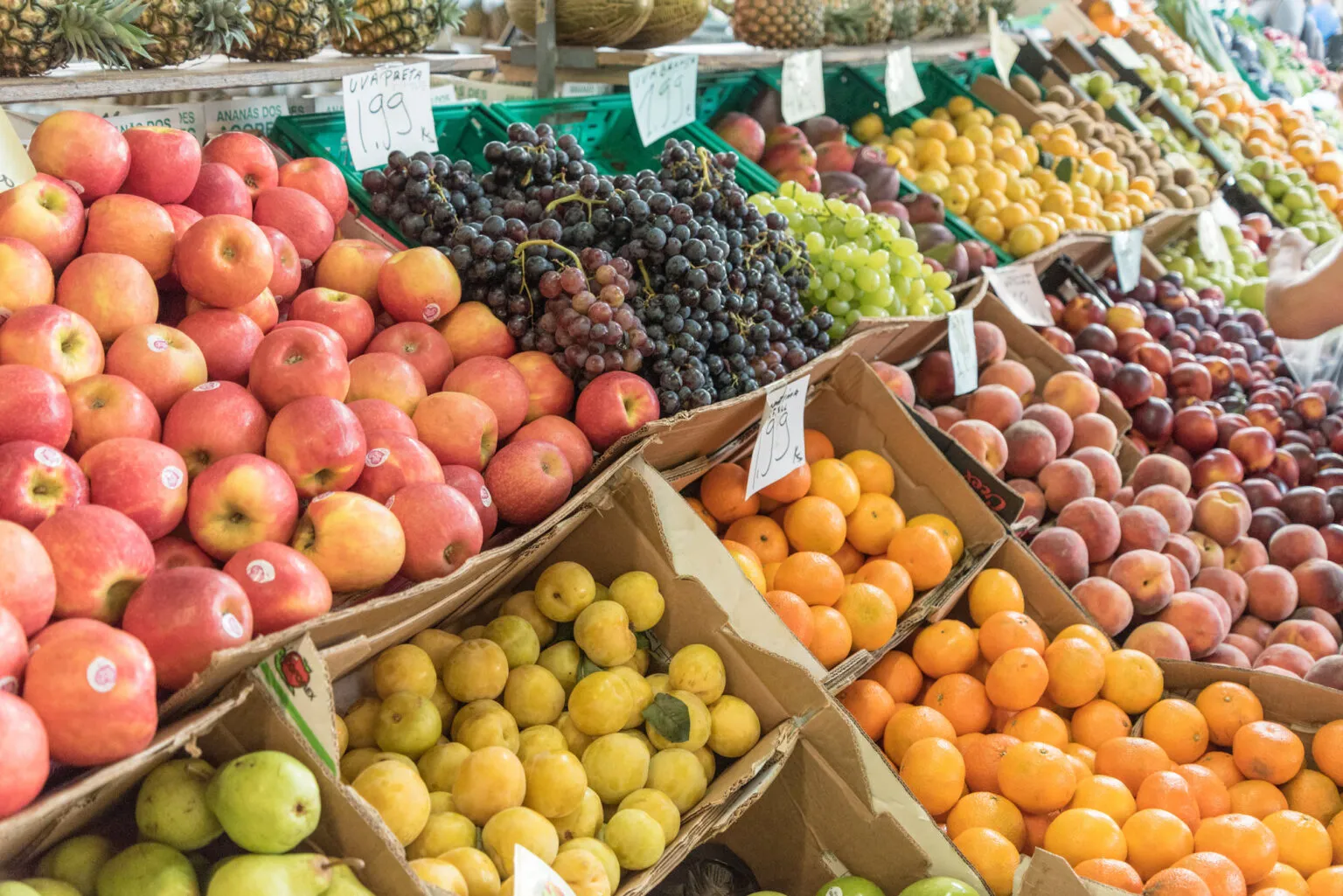 Kleurrijke marktkraam boordevol vers fruit zoals rode appels, donkere druiven, citrusvruchten en perziken in kartonnen dozen op een markt in de Azoren