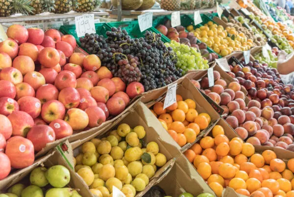 Kleurrijke marktkraam boordevol vers fruit zoals rode appels, donkere druiven, citrusvruchten en perziken in kartonnen dozen op een markt in de Azoren