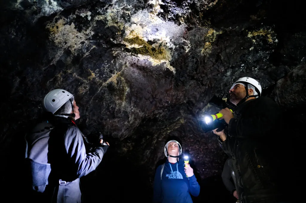 Een groep speleologen met helmen en zaklampen schijnt op de donkere rotswanden en het plafond van een vulkanische grot op de Azoren.
