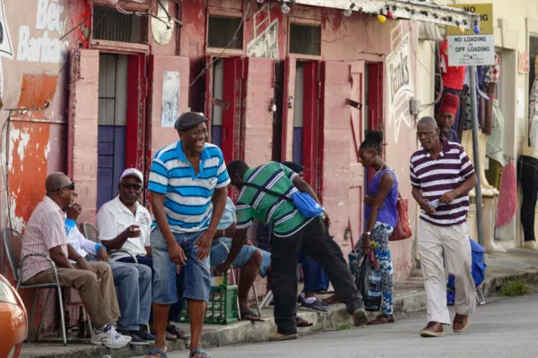 Sfeervol straatbeeld in Bridgetown op Barbados, waar lokale bewoners praten, lachen en wandelen op de stoep voor kleurrijke winkelgevels.