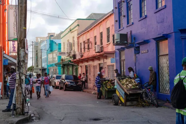 Mensen lopen langs kleurrijke historische gebouwen en marktkraampjes in een levendige straat van Bridgetown op Barbados.