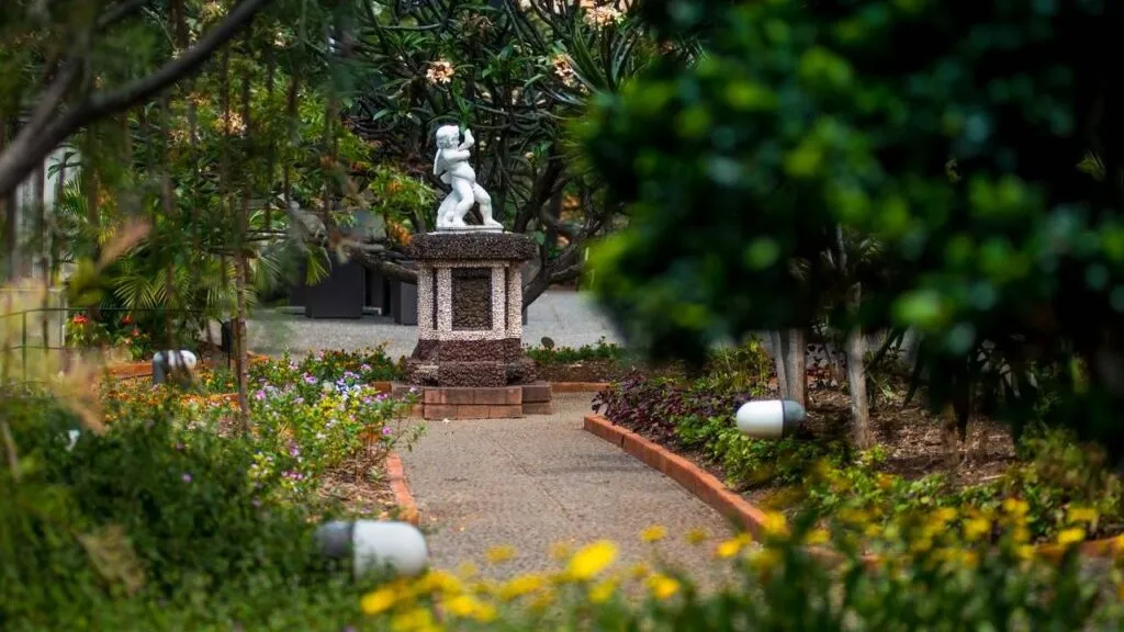 Een rustig wandelpad door een groen ingerichte binnentuin op Madeira, met gele bloemen en een klassiek standbeeld in het midden.