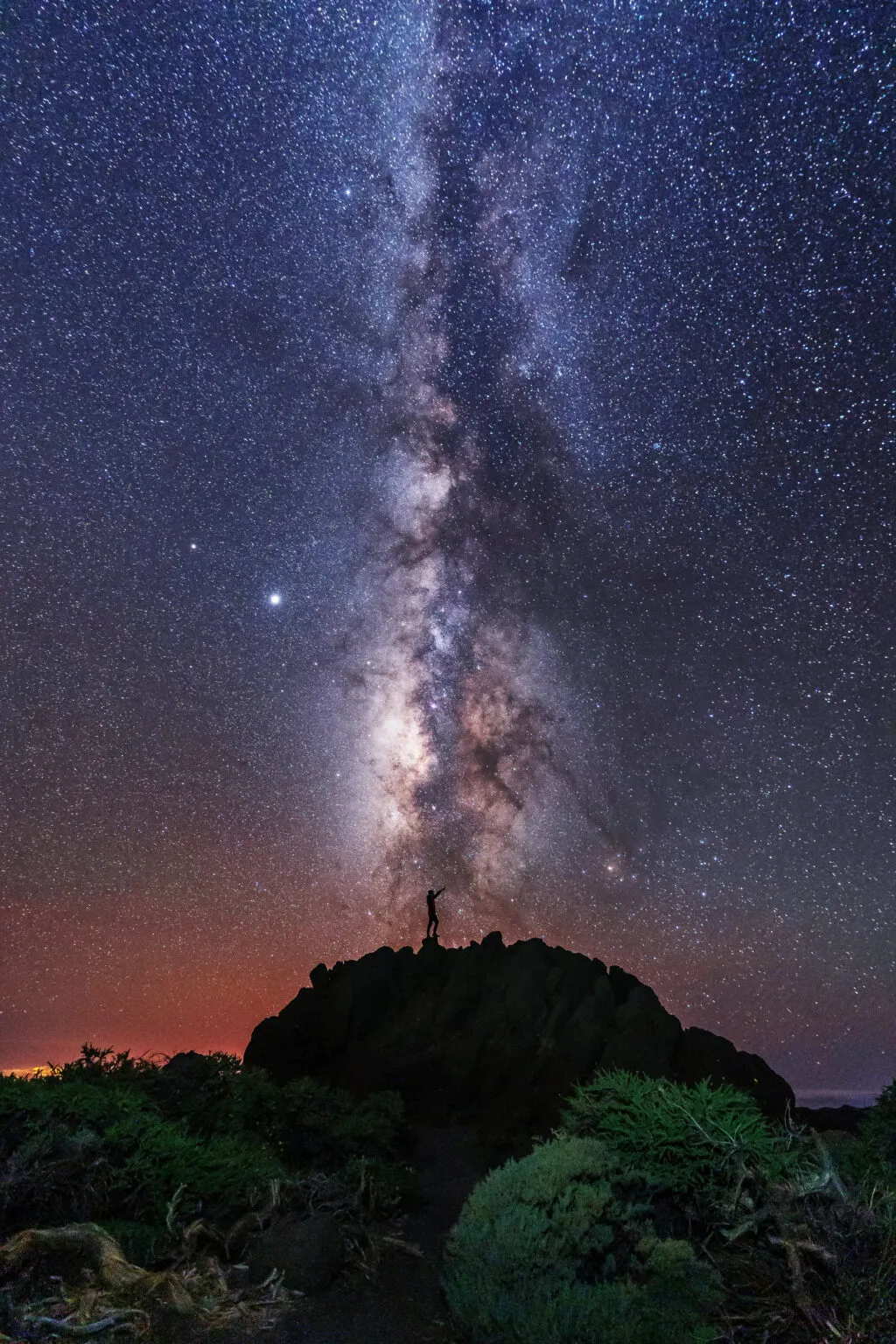 Een heldere nachthemel vol sterren waarin de Melkweg verticaal oprijst vanuit het donkere silhouet van een bergtop op La Palma.