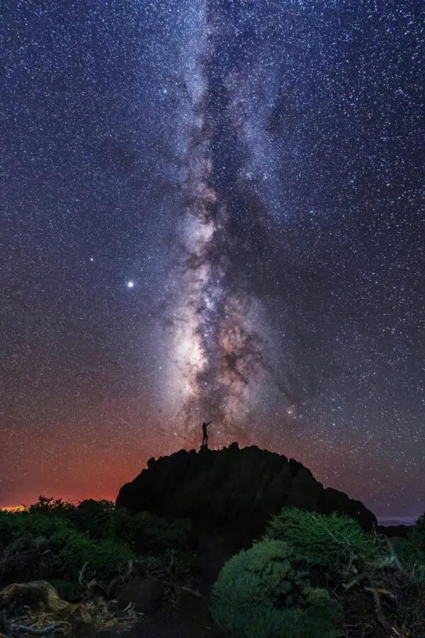 Een heldere nachthemel vol sterren waarin de Melkweg verticaal oprijst vanuit het donkere silhouet van een bergtop op La Palma.