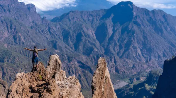 Wandelaar staat met de armen spreid op een rots top bij een uitkijkpunt, uitkijkend over de imposante bergen van Nationaal Park Caldera de Taburiente op La Palma.